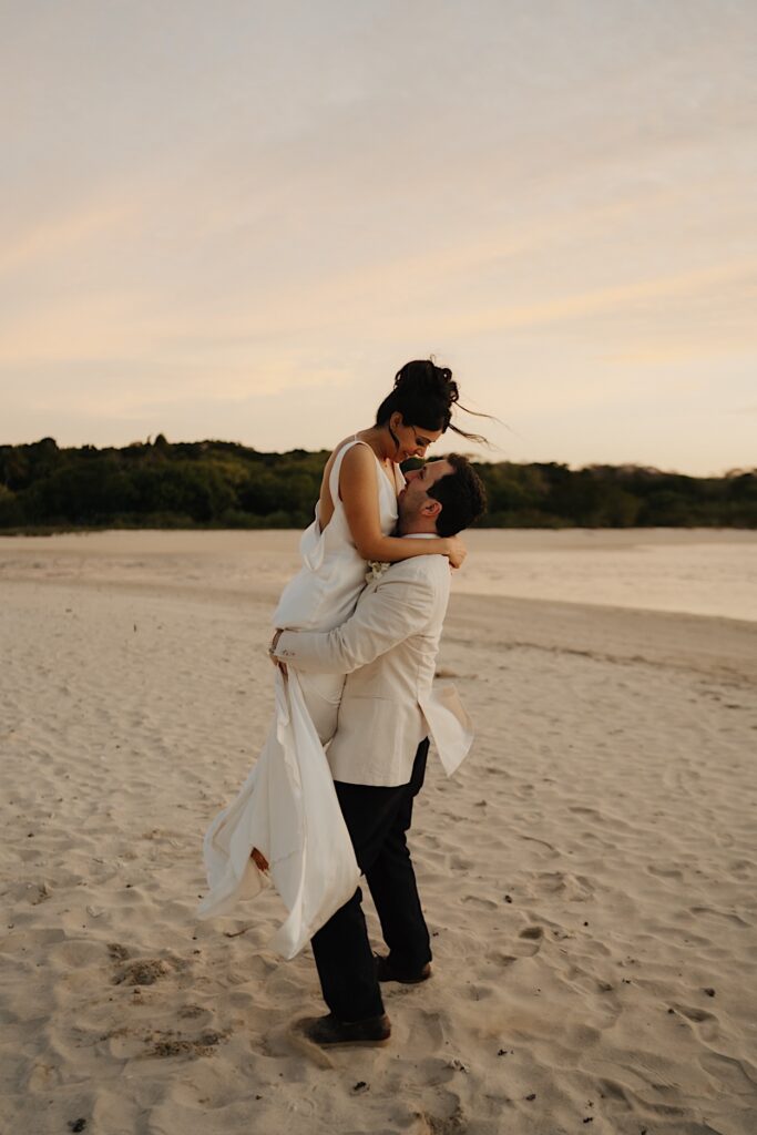 207_couple-embracing-beach-wedding-fiji Couple embracing on the beach during their wedding in Fiji, with the groom lifting the bride in a joyful moment
