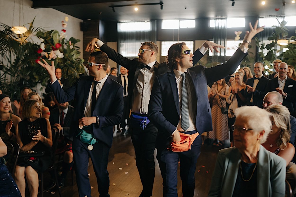 068_groomsmen-entering-ceremony-glasshaus-brucke-wedding-melbourne Groomsmen entering the ceremony at the Glasshaus Brucke wedding in Melbourne, throwing flowers out of bum bags, creating a hilarious moment