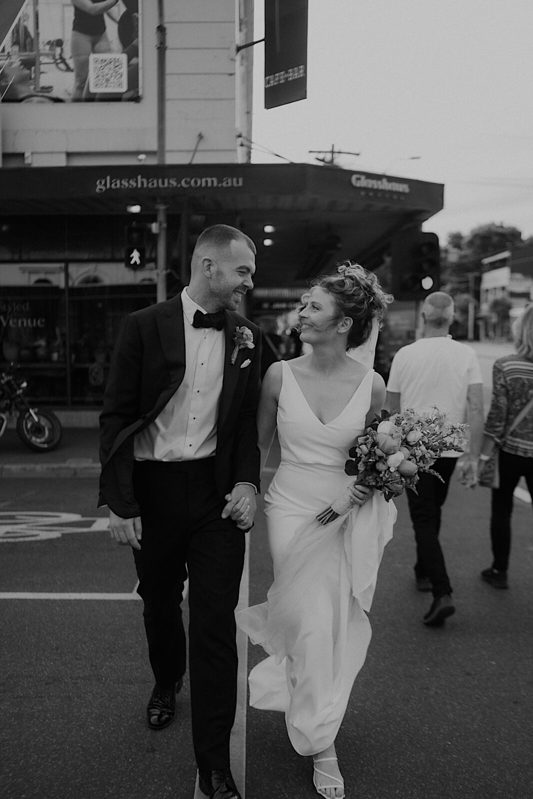 131_couple-portraits-outside-glasshaus-wedding-melbourne Black and white portrait of the couple walking hand-in-hand across a pedestrian crossing during their wedding in Melbourne