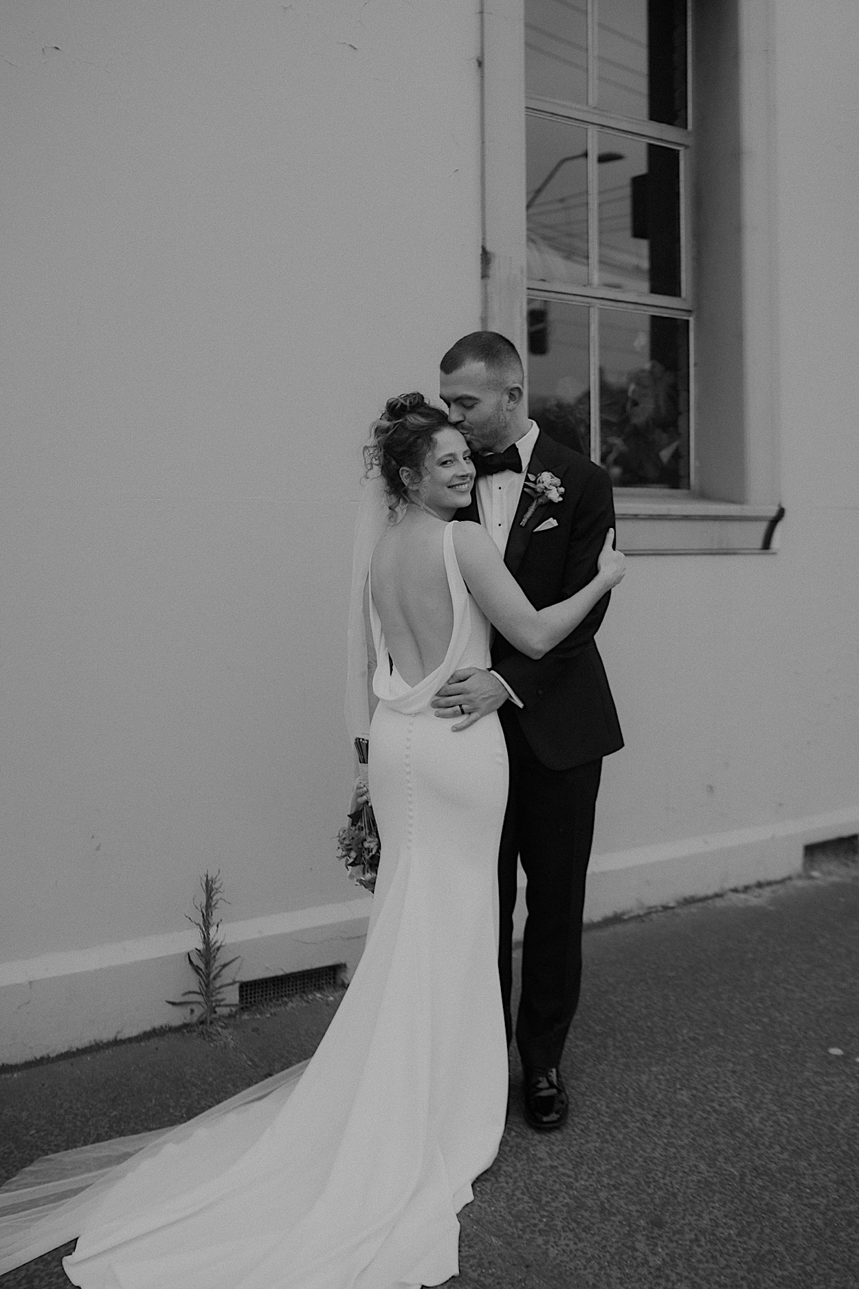 137_couple-portraits-after-glasshaus-brucke-ceremony-melbourne Black and white portrait of the bride’s dress from the back, as she stands with the groom after their wedding ceremony at Glasshaus Brucke in Melbourne