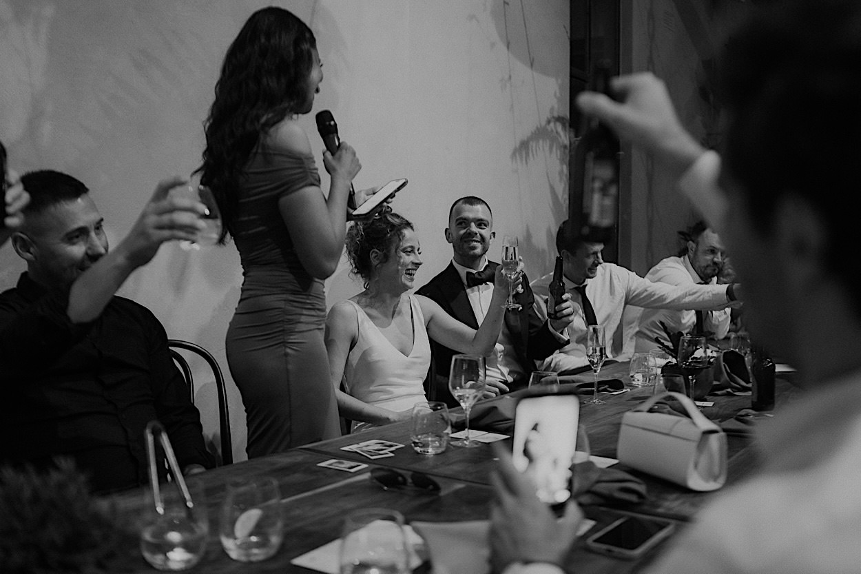 183_speeches-wedding-reception-at-glasshaus-brucke-richmond Bride and groom cheering during the maid of honor's speech at their wedding reception at Glasshaus Brucke in Richmond