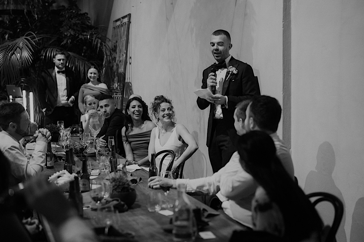 185_groom-speech-wedding-reception-at-glasshaus-brucke-melbourne Black and white photo of guests listening to the groom's speech during a wedding reception at Glasshaus Brucke in Melbourne