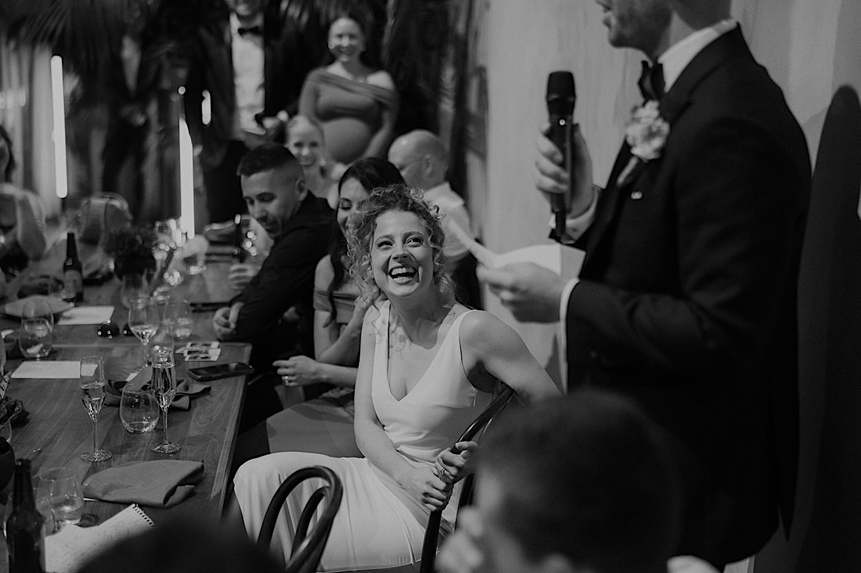 187_bride-laughing-speech-glasshaus-brucke-melbourne-wedding Black and white photo of the bride laughing during a speech at a wedding reception at Glasshaus Brucke in Melbourne