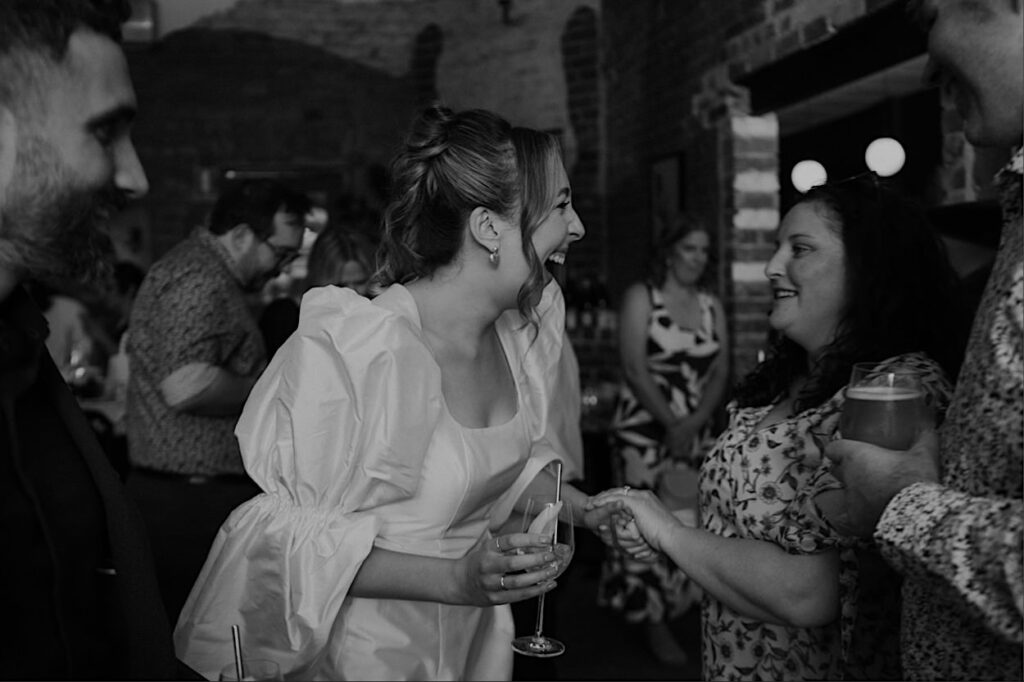 150_bride-candid-maggies-snacks-and-liquor-wedding Black and white photo of the bride candidly smiling during the reception at Maggie’s Snacks and Liquor.