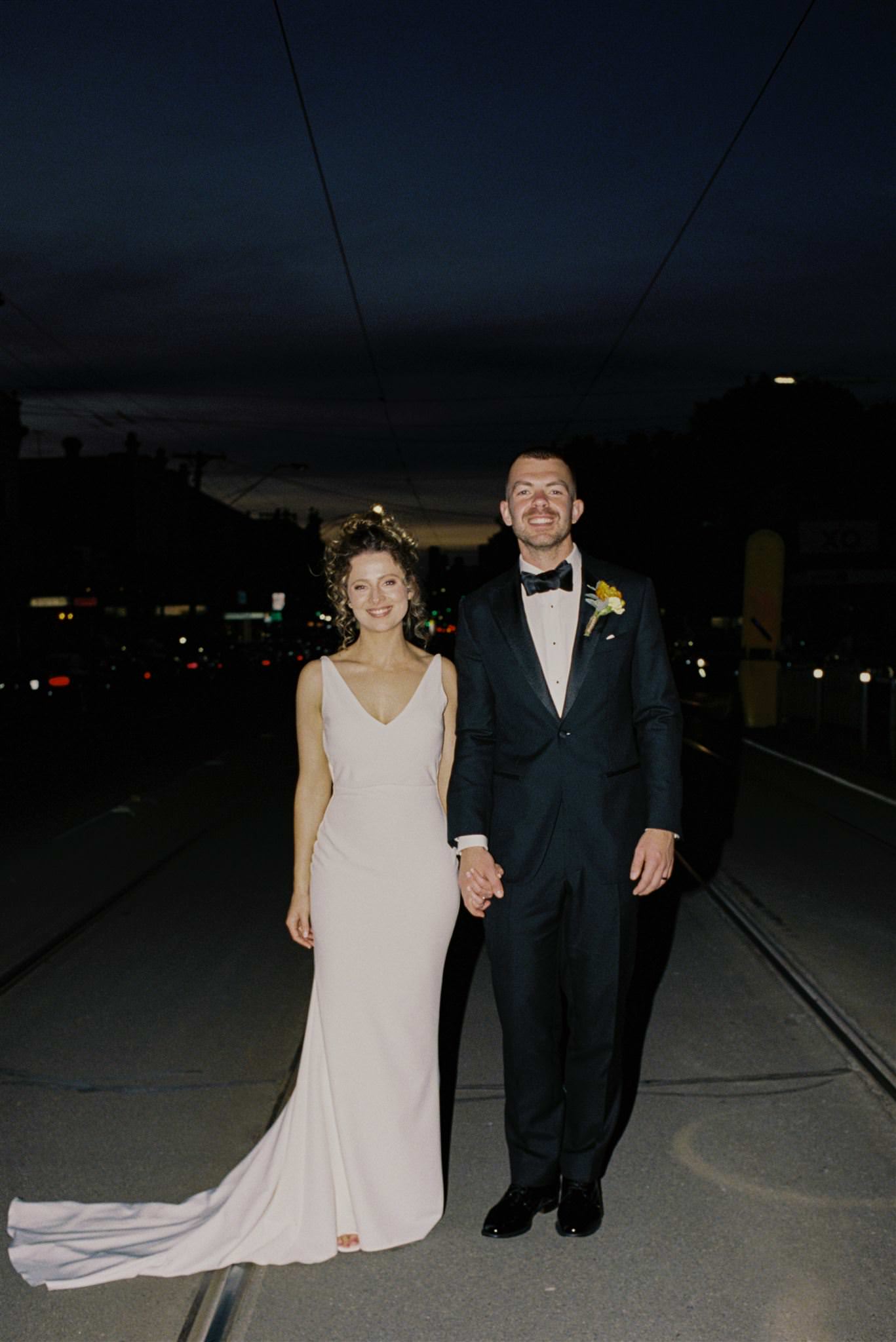35mm-film-glasshaus-brucke-night-portrait-richmond 35mm film photo of a newlywed couple at Glasshaus Brücke in Richmond, standing on tram tracks for a nighttime portrait