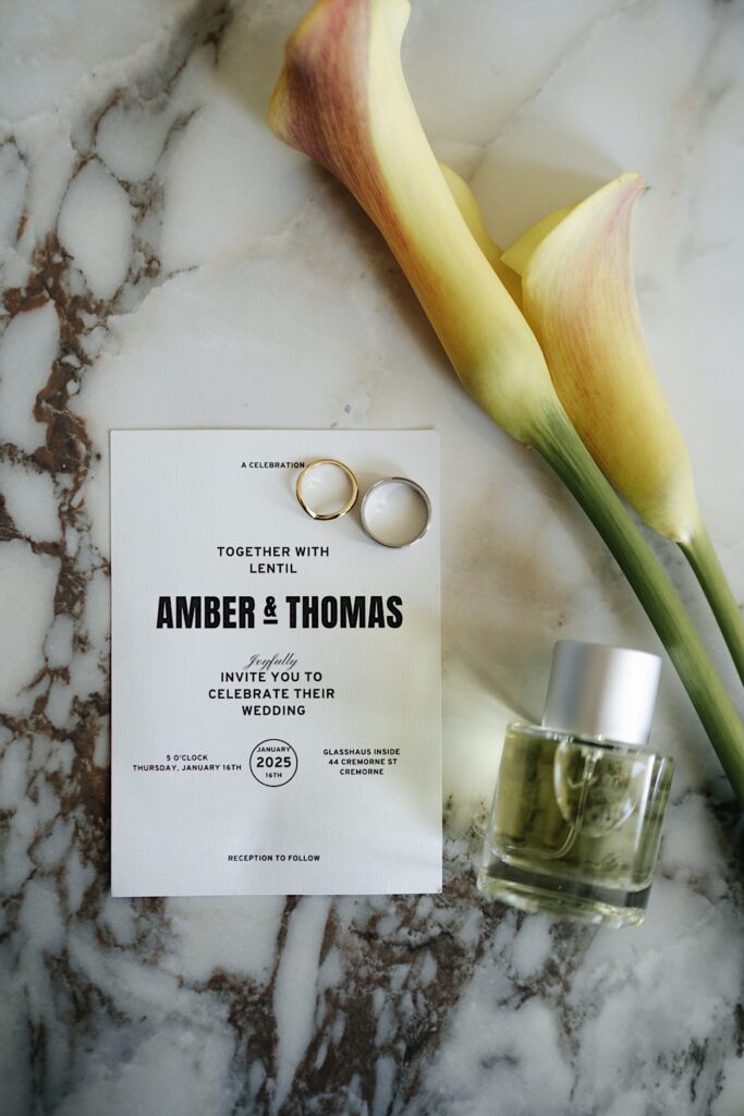 Yellow lilies, wedding rings, invitation, and perfume details before the Glasshaus Inside wedding in Cremorne, Melbourne