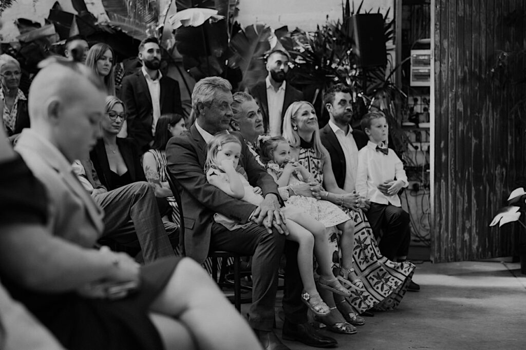 Black and white photo of wedding guest attentively listening to the celebrant’s speech during Glasshaus Inside ceremony in Melbourne