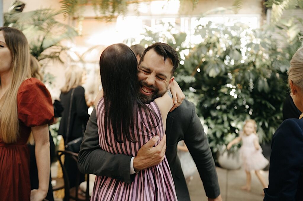 The groom hugs a guest during their Glasshaus Inside wedding in Cremorne.