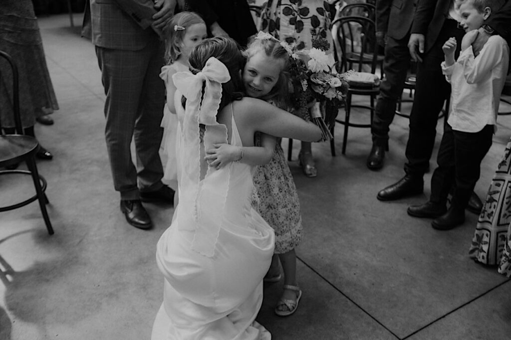 Black-and-white photo of the bride hugging the flower girl during their Glasshaus Inside wedding ceremony in Cremorne.