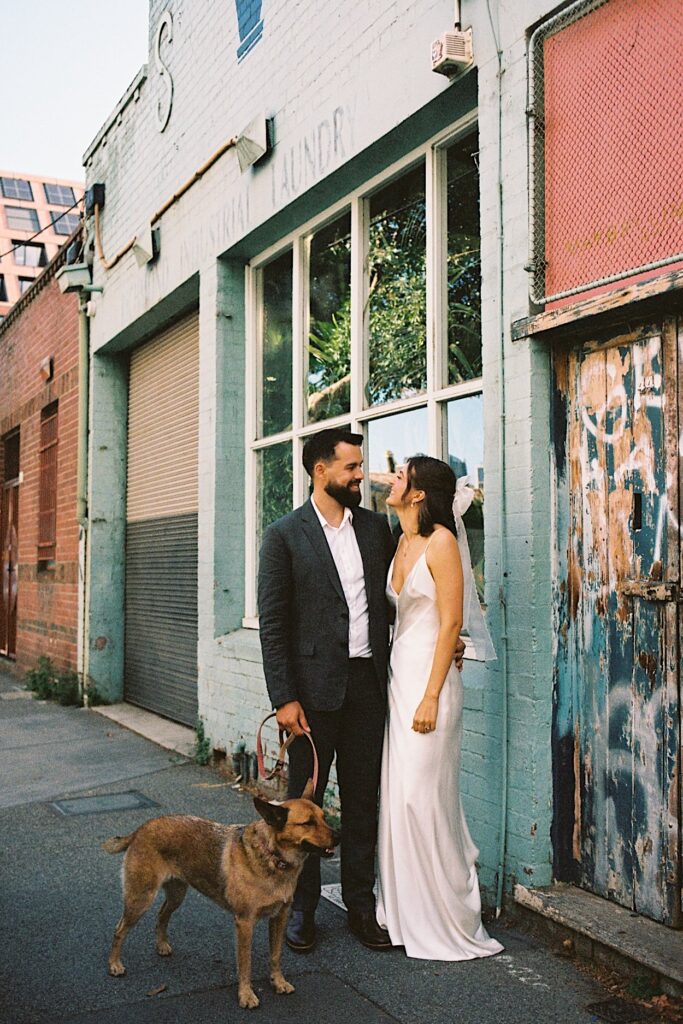 The couple poses for portraits outside the venue with their dog during their Glasshaus Inside wedding in Melbourne, captured on 35mm film.