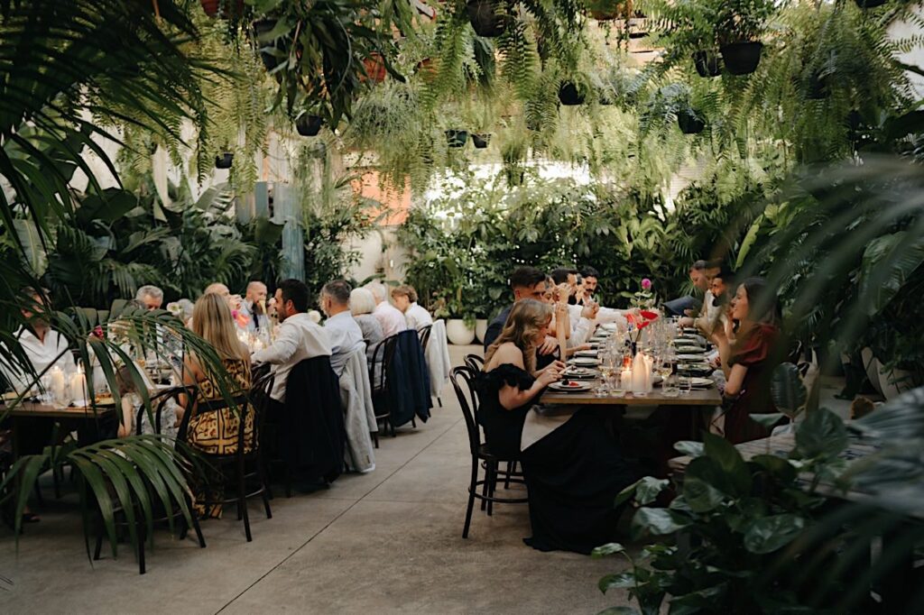 Wide shot of wedding guests seated at tables surrounded by lush greenery during a Glasshaus Inside wedding reception in Cremorne, Melbourne.
