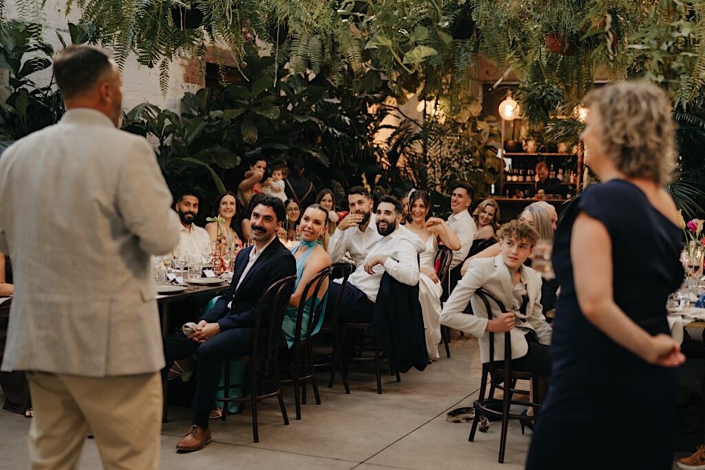 View from behind the speaker showing guests attentively watching during a wedding speech at a Glasshaus Inside wedding in Cremorne.