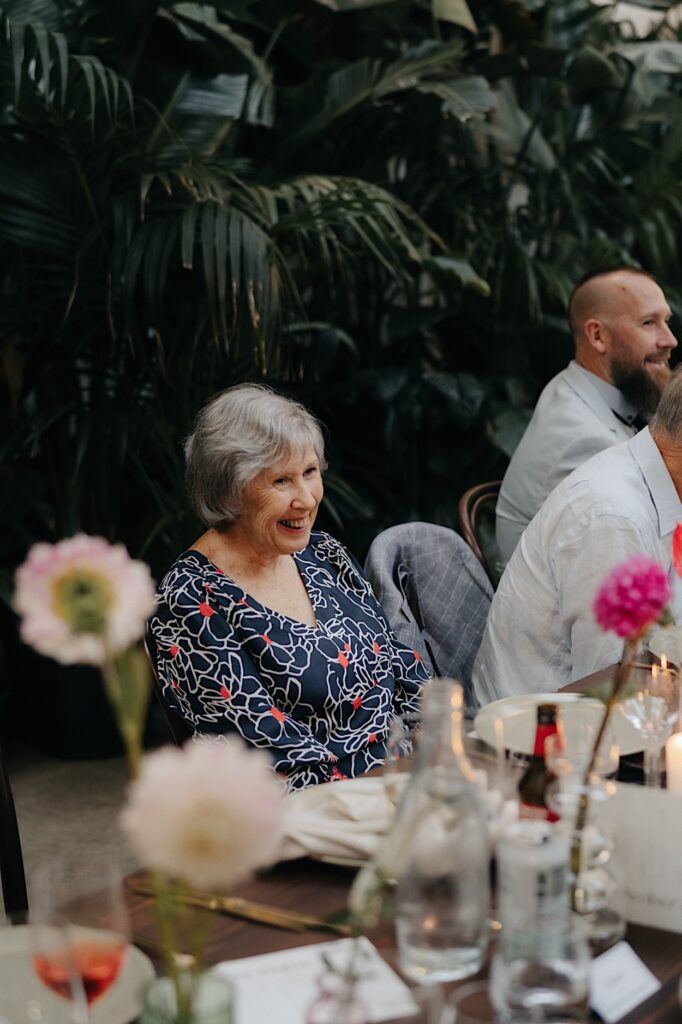 A guest smiling during speeches at a Glasshaus Inside wedding reception.