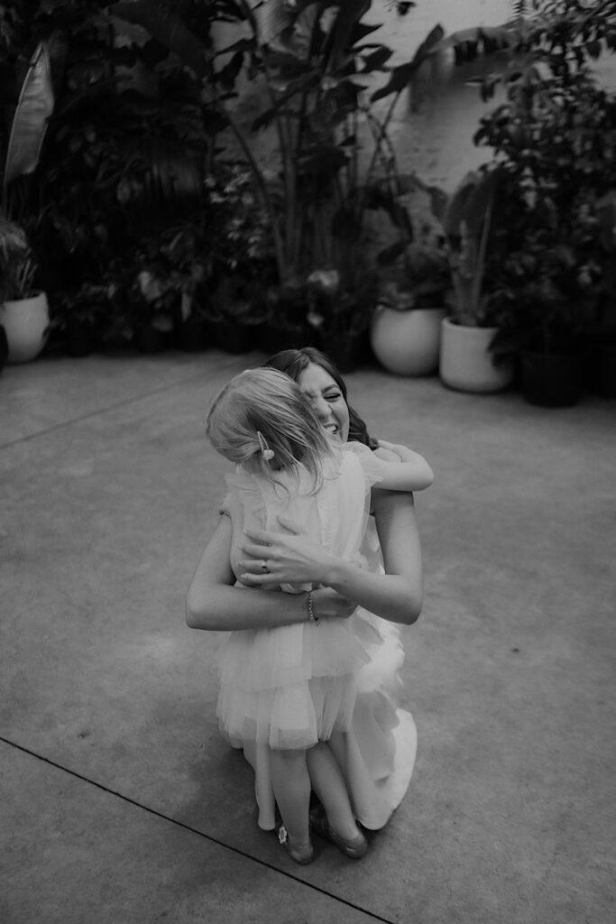 Black-and-white photo of the bride hugging the flower girl during a Glasshaus Inside wedding.